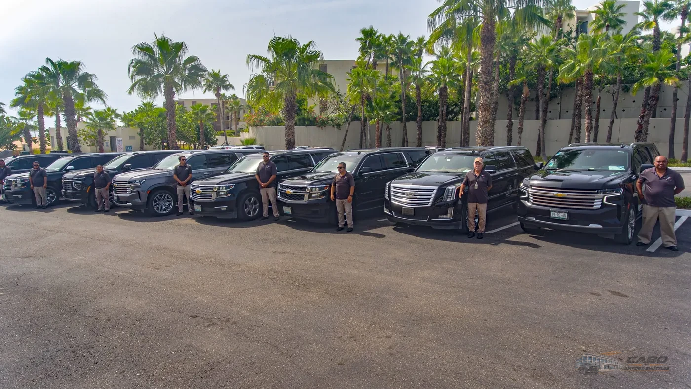 Los Cabos shuttle drivers standing beside a fleet of black SUVs.